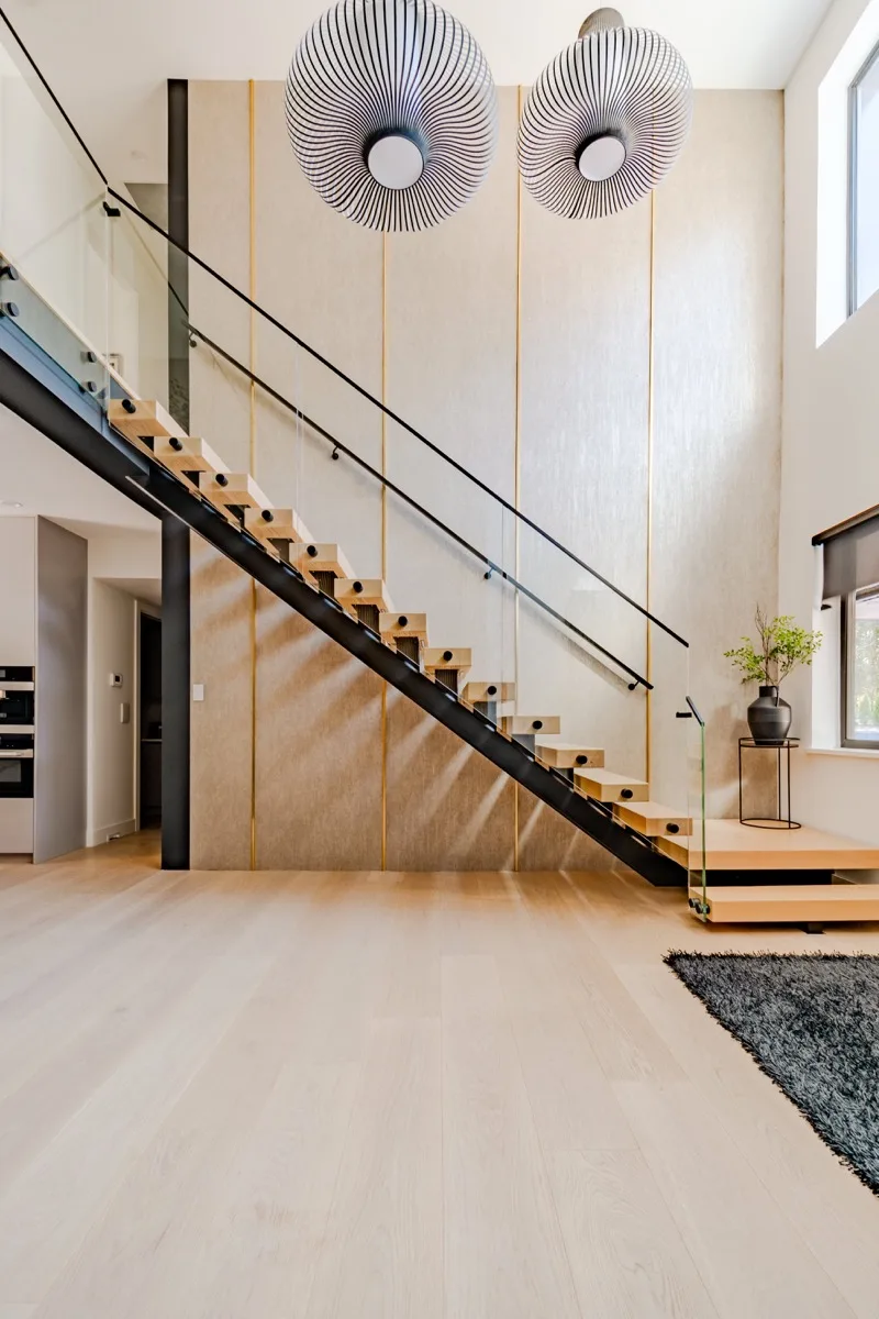Luxury home foyer real estate photography Vancouver, floating open-tread staircase with black steel stringer and glass railing, double Vertigo pendant lights, double-height ceilings, and wide-plank oak floors