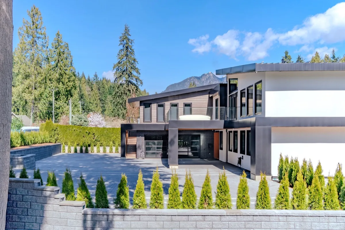 Modern luxury home exterior real estate photography Vancouver, dark charcoal and cedar facade, large glazing, paver driveway, columnar trees, cedar hedging, and snow-capped mountain backdrop