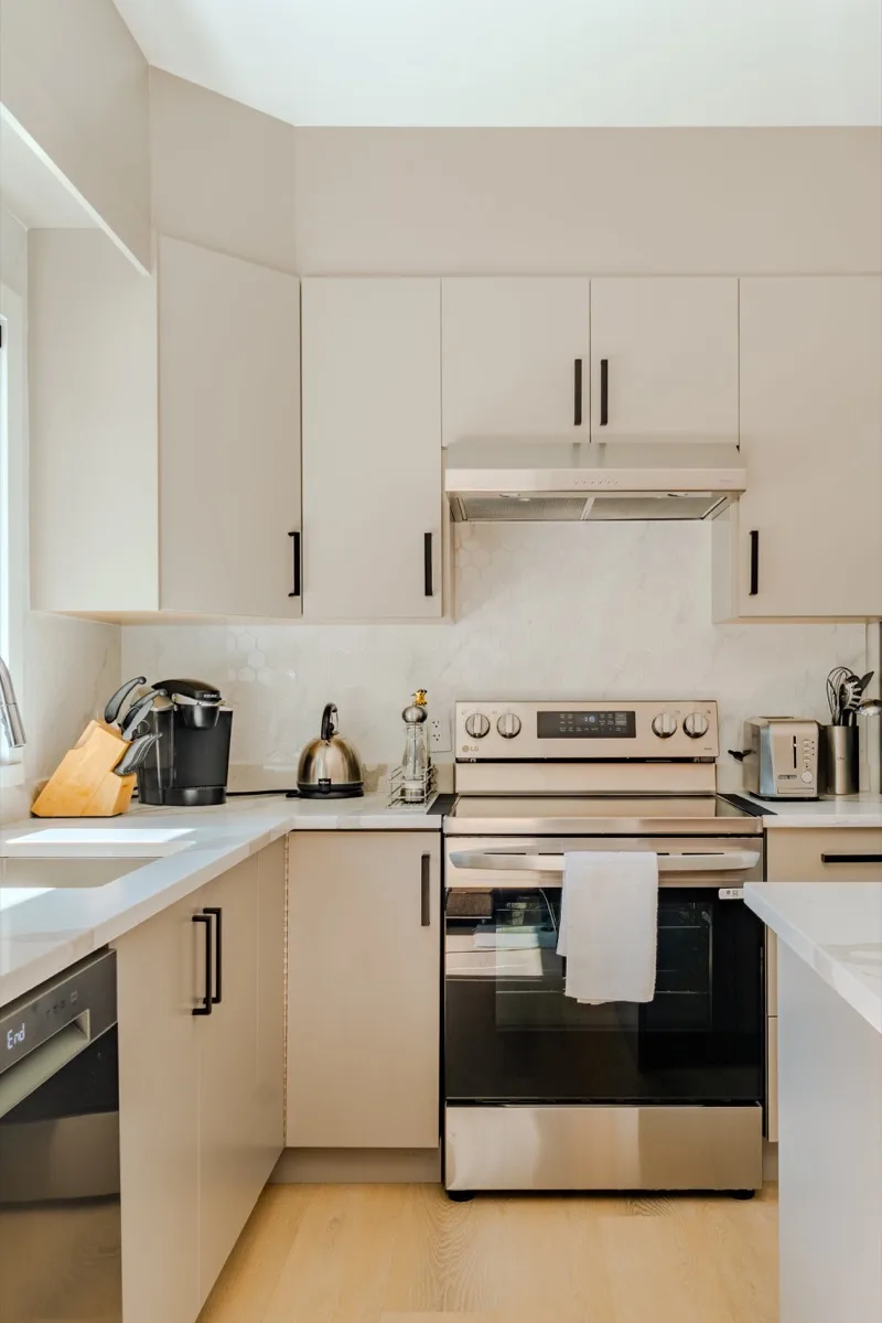 Modern kitchen real estate photography Vancouver, cream flat-front cabinetry with matte black hardware, white quartz countertops, marble-look tile backsplash, and stainless steel appliances