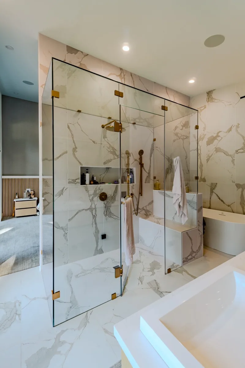 Luxury ensuite real estate photography Vancouver, full-height book-matched Calacatta marble tile, frameless glass shower enclosure with brushed gold hardware, integrated marble bench, and undermount tub